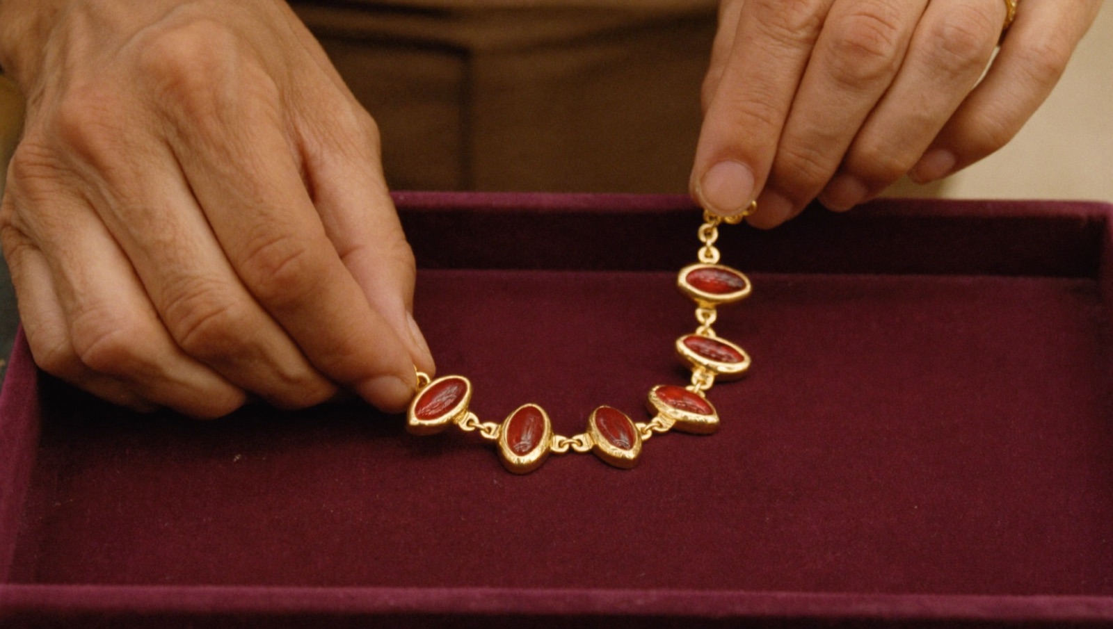 Illustrative image of hands arranging a necklace on velvet